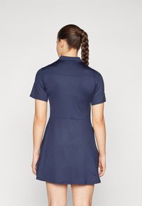 Mornarska haljina kratkih rukava sa strukturiranim kragnom i teksturiranim materijalom. Sadrži uski struk i lepršavu suknju, s glatkim završetkom.