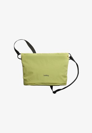 Sac messager en tissu vert avec une finition texturée, bandoulière noire réglable et marquage discret. Il présente une fermeture éclair et un design minimaliste.