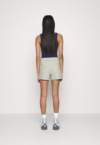 Shorts en coton gris avec une large ceinture, associés à un débardeur sombre. Le mannequin porte des chaussettes blanches et des baskets grises avec un motif d'étoile.
