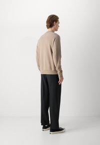 Felpa beige con colletto e polsini a coste, abbinata a pantaloni neri larghi e sneakers nere classiche, vista da dietro.
