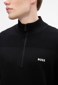 Μαύρος φερμουάρ σκούφος με υφή ριμπ σχεδίαση στο άνω μέρος και λευκό λογότυπο "BOSS" στο αριστερό στήθος.