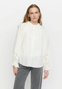 Weiße Bluse mit Knöpfen und gerafftem Ausschnitt sowie filigranem Spitzenbesatz an den Ärmeln. Hergestellt aus leichtem Stoff mit langen, schwingenden Ärmeln.