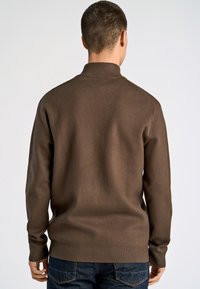 Brauner Strickpullover mit hohem Kragen und gerippten Bündchen, der eine glatte Textur und eine figurnahe Passform aufweist, getragen mit blauen Denim-Jeans.