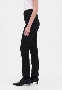 Črne kavbojke iz jeansa s prilegajočo obliko, srednje visokim pasom in slogom s petimi žepi. Kombinirane z ostro črnimi petami.