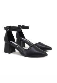 Scarpe nere in pelle con tacco alto, punta affusolata, cinturino alla caviglia e tacco a blocco. Texture liscia con un design minimalista.