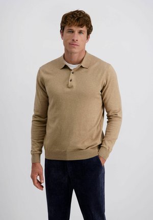 Tan polo trui met drie knopen, geribbelde manchetten en zoom. Draagt met donkere corduroy broek met verticale strepen, wat de textuurcontrast benadrukt.