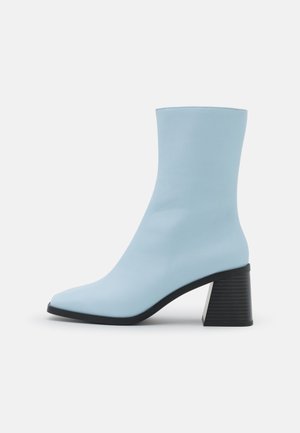 Bottine bleu clair en matériau lisse, dotée d'une pointe effilée et d'un talon bloc noir sculpté avec une texture côtelée.