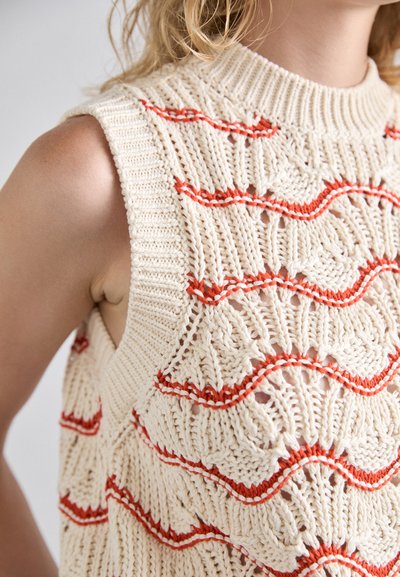 Pull sans manches en crème avec des rayures rouges ondulées. Présente des motifs de points texturés et un col rond côtelé.