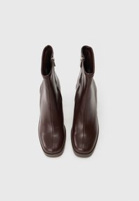 Botine din piele maro, cu o textură netedă, vârful pătrat și fermoare laterale, plasate pe un fundal alb.