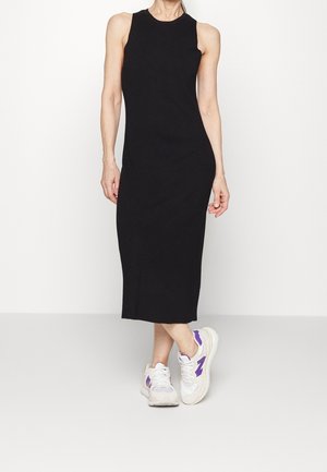 Vestido midi negro sin mangas con un escote redondeado. Se lleva con zapatillas blancas con detalles en púrpura. Textura suave, silueta ajustada.