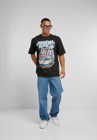 Czarny graficzny t-shirt z kolorowym wzorem wyścigowym i napisem "Market Racing", w połączeniu z jasnoniebieskimi dżinsami i białymi trampkami.
