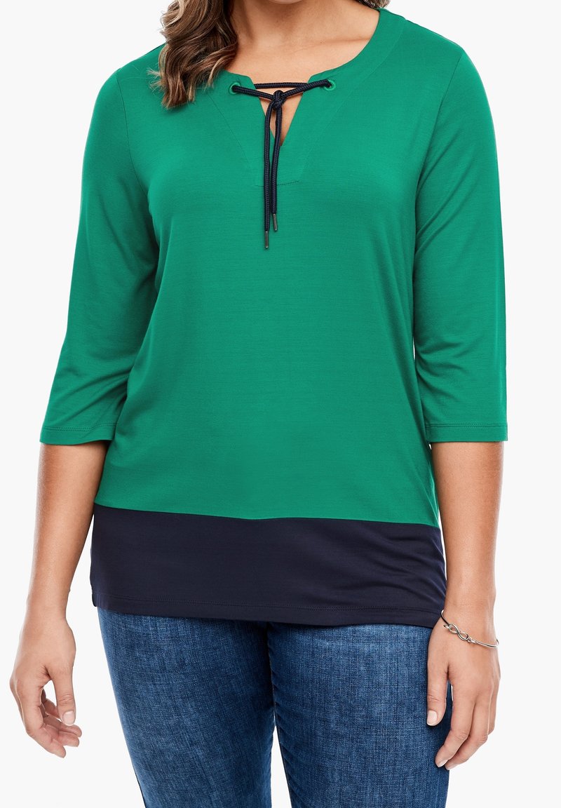 Top verde a maniche lunghe con scollatura a V e parte inferiore blu navy. Presenta un dettaglio con lacci sul collo e una texture liscia.