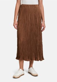 Jupe plissée marron avec une taille élastique, arrivant mi-mollet, portée avec des baskets blanches ornées de accents gris et beige.