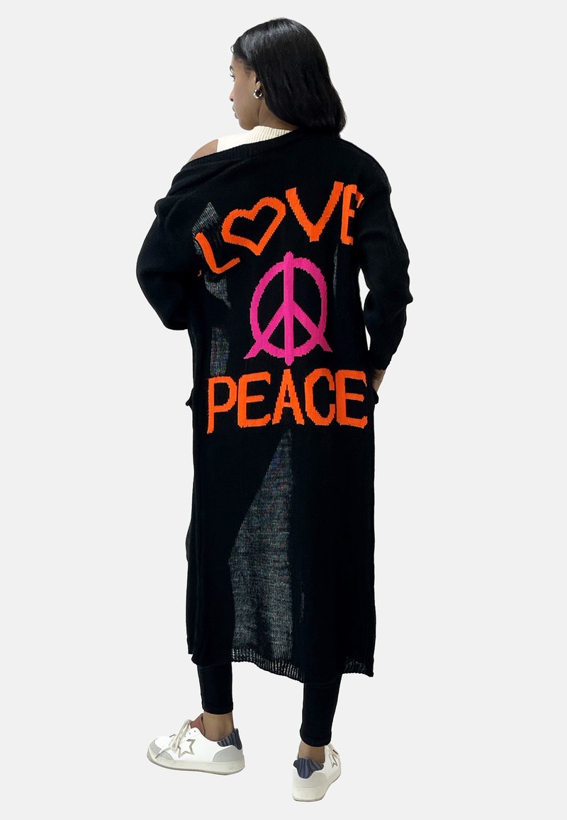 Lång svart cardigan med ljus orange och rosa text som säger "KÄRLEK" och "FRID", med en löst stickad textur och öppen design.