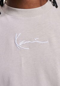 Light gray t-shirt made of soft fabric, featuring a round neckline and a white embroidered logo across the chest.