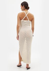 Abito in maglia con un motivo a righe bianche e beige, caratterizzato da un design incrociato sulla schiena e una spaccatura alta fino alla coscia per un tocco in più.