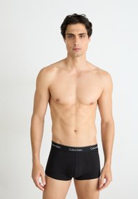 Zwarte katoenen boxershorts met een eenvoudige uitstraling, voorzien van een gestreepte tailleband met daarin de opdruk "Calvin Klein" in witte letters.