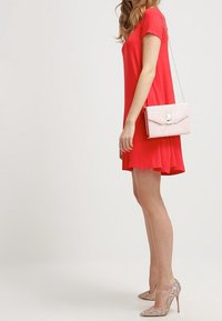 Robe rouge à manches courtes avec un ourlet évasé, associée à un sac à main pailleté rose et des escarpins beiges étincelants. Tissu lisse, design décontracté.