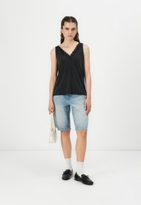 Top nero senza maniche con bordo in pizzo, abbinato a pantaloni bermuda in denim azzurro chiaro. Gli accessori includono una borsa bianca e scarpe nere con calzini.