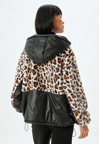 Leopardmønstret fleecejakke med sort pufferstof i den nederste del og hætten, med elastiske manchetter og kant for justerbar pasform.