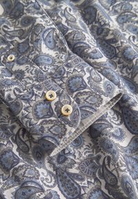 Camicia con bottoni caratterizzata da un motivo paisley in tonalità di blu e grigio. Realizzata in un tessuto dalla texture liscia, decorata con bottoncini chiari.