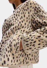 Umělá kožešinová bunda v světle béžové barvě s černým skvrnitým vzorem, s kulatým límcem, dvěma velkými knoflíky a bočními kapsami.