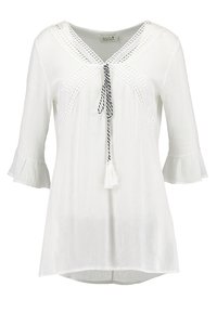 Blusa bianca con maniche flare a 3/4, scollo a V e decorazioni in pizzo. Presenta un cordoncino con pompon nei colori nero e bianco.