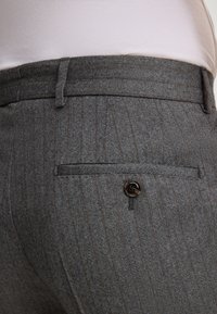 Pantaloni grigi a spina di pesce con una delicata riga verticale, dotati di una tasca posteriore chiusa da un bottone scuro e una vita dritta.