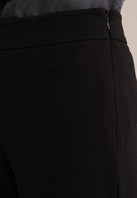 Svarta skräddarsydda byxor med en mjuk textur, som har ett diskret mönster, sidodragkedjestängning och en figurnära design.