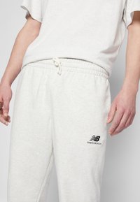 Pantaloni jogger grigi chiari realizzati in tessuto morbido, dotati di vita elastica con cordino e del logo "New Balance" nero sul lato.