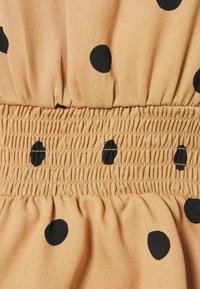 Beige tyg med svarta prickar, med en sammetsliknande elastisk midjeresår som har veck.