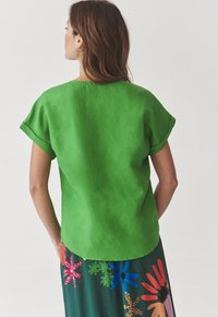 Top verde a maniche corte con una vestibilità rilassata e orli arrotolati, realizzato in tessuto morbido, abbinato a una gonna con motivo floreale multicolore.