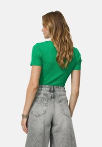 Haut vert à manches courtes avec une texture côtelée, associé à un pantalon en denim gris taille haute avec une finition délavée et des poches arrière.