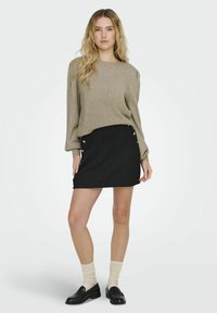 Ljusbrun stickad tröja med långa ärmar, i kombination med en svart ribbad kjol med silverfärgade knappdekorationer längs sidan. Svarta loafers och ljusa strumpor.