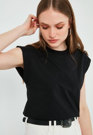 T-shirt en coton noir à manches courtes retroussées, col rond et coupe décontractée, associé à une ceinture noire avec une boucle décorative.