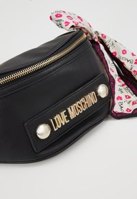 Czarna skórzana nerka z złotym zamkiem i wyraźnym logo. Posiada dekoracyjną różowo-białą chustę w wzory zawiązaną do zamka.