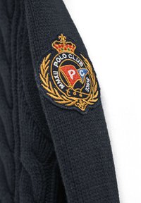Granatowy sweter dziergany z teksturowanym wzorem oraz złotą naszywką z haftem przedstawiającym koronę i logo "Polo Club" na lewym ramieniu.