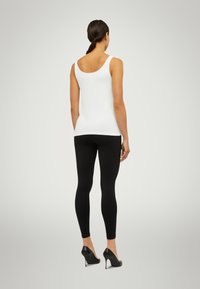 Vit linne, svarta leggings, högklackade skor. Slät tyg, figurnära design. Bakifrån framhäver silhuetten och rena linjer.
