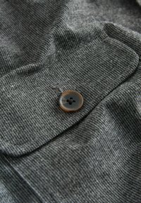 Grau strukturiertes Gewebe mit einem Knopfdetail in einem braun-schwarzen Marmordesign, das subtile Rillen und Falten im Material zeigt.