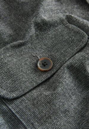 Szary, teksturowany materiał z detalem guzika w brązowo-czarnym marmurkowym wzorze, ukazujący subtelne fałdy i wgłębienia w materiale.