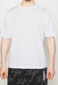 Vit t-shirt med kort ärm, gjord av syntetiskt material, med en liten, präglad logga. Rund halsringning med slät textur och avslappnad passform.