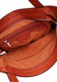 Atvērts sarkanas ādas soma interjers ar oranžu auduma oderi, rāvējslēdzēja kabatu un iekšējo kabatu.