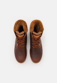 Bruna läderstövlar med hög topp, fuskpälsfoder, rund tå, snörning fram och gummisula. Texturerat material och varm färgskala.