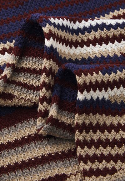 Coperta in maglia a motivo zigzag con colori rosso scuro, crema, blu navy e grigio. Texture morbida con un aspetto stratificato.