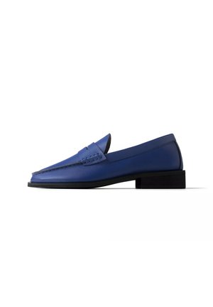 Blauwe leren loafer met lage zwarte hak en gestikte details op het bovenwerk, zijaanzicht op een witte achtergrond.