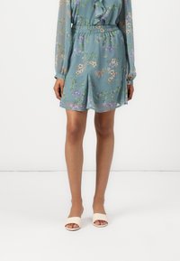 Blomstrede shorts i lysegrønt stof med elastisk talje. Gennemsigtig tekstur med en afslappet pasform og sidelommer. Parret med lyse sandaler.