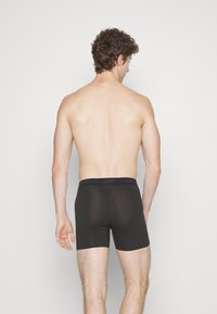 Zwarte katoenen boxershorts met een paarse Calvin Klein merkband. Een gladde textuur en een getailleerd ontwerp, weergegeven vanaf de achterkant.