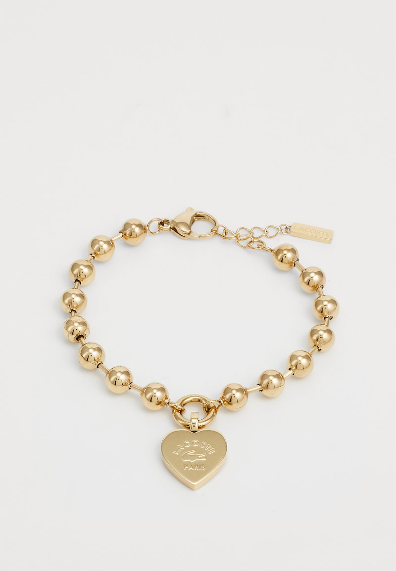 Kuldne käevõru, millel on ümarad helmed, südamekujulise ripatsi koos reljeefse logoga ja kindel lukustus koos reguleeritava ahelaga.