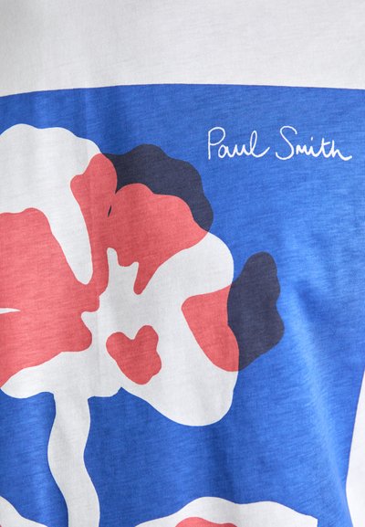 Kokvilnas T-krekls ar florālu dizainu sarkanā, baltā un jūras zilā krāsā uz zila fona. Paraksts "Paul Smith" angļu rakstībā augšējā daļā.