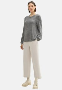 Top de manga larga con un patrón de zigzag en blanco y negro, combinado con pantalones anchos color beige y zapatos gruesos de color crema. Tejido texturizado, corte relajado.
